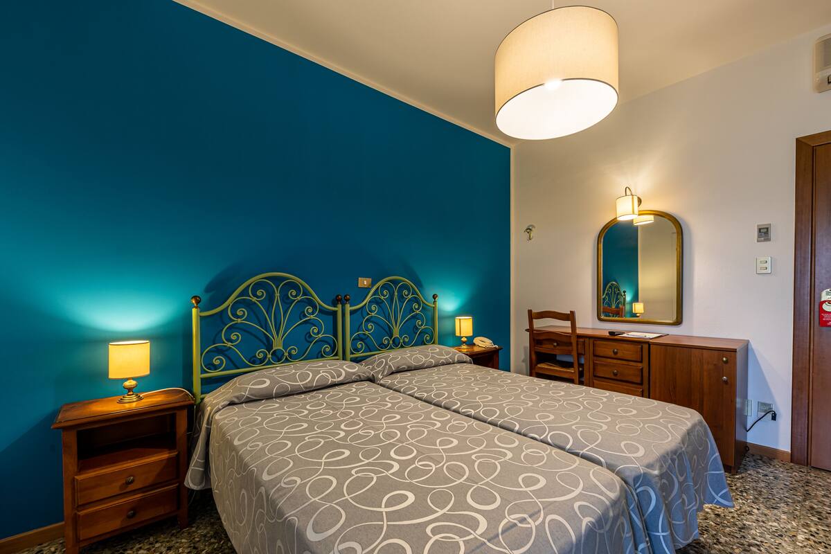 Une chambre d’hôtel avec un lit, des tables de chevet, une commode et un miroir.