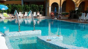 A swimming pool with clear blue water, tiled steps, and lounge chairs around the perimeter. - Hotel Bisesti (Garda)