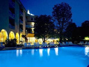 Un hotel con piscina, sillones de descanso y un árbol al fondo.