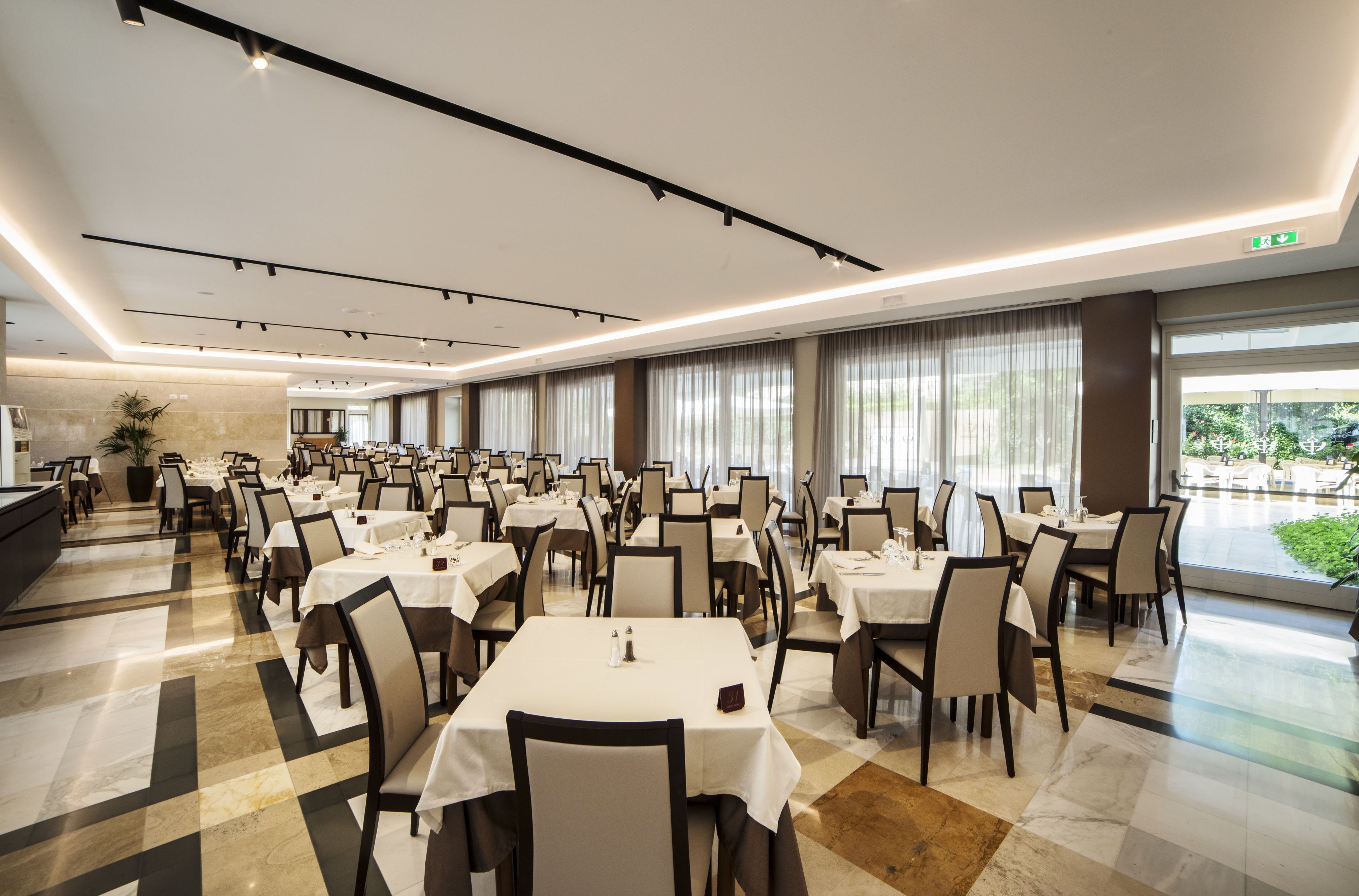 A spacious dining area with multiple tables and chairs, large windows with curtains, and a clean, modern design.