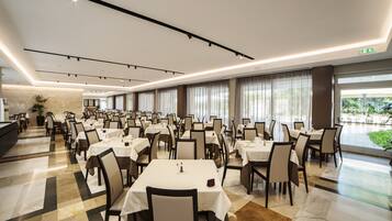A spacious dining area with multiple tables and chairs, large windows with curtains, and a clean, modern design.