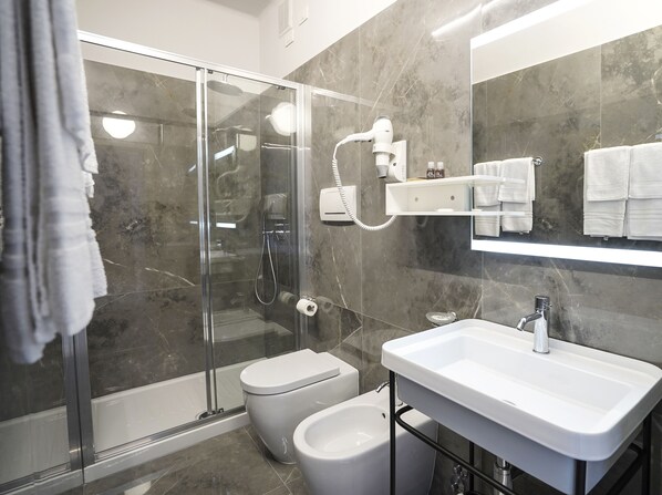 A modern bathroom with a glass shower enclosure, a toilet, a bidet, and a sink with a mirror above. - Hotel Sole Mare (Ventimiglia)