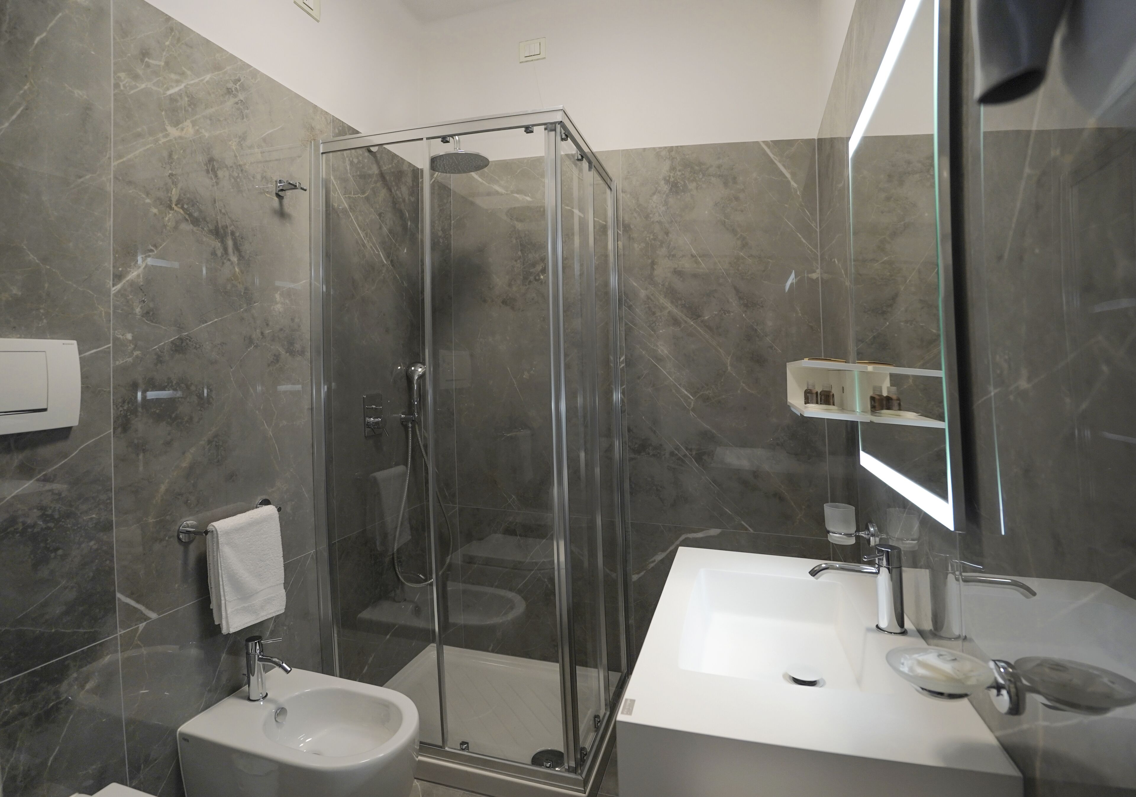 Un baño moderno con ducha envuelta en vidrio, lavamanos sobre pedestal y un espejo grande.