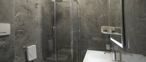 Ein modernes Badezimmer mit einer Glaskabine zur Dusche, einem Standwaschbecken und einem großen Spiegel.