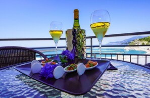 A table with a bottle of wine, two glasses of wine, and a plate with food and flowers on a balcony overlooking a beach. - Hotel Sole Mare (Ventimiglia)