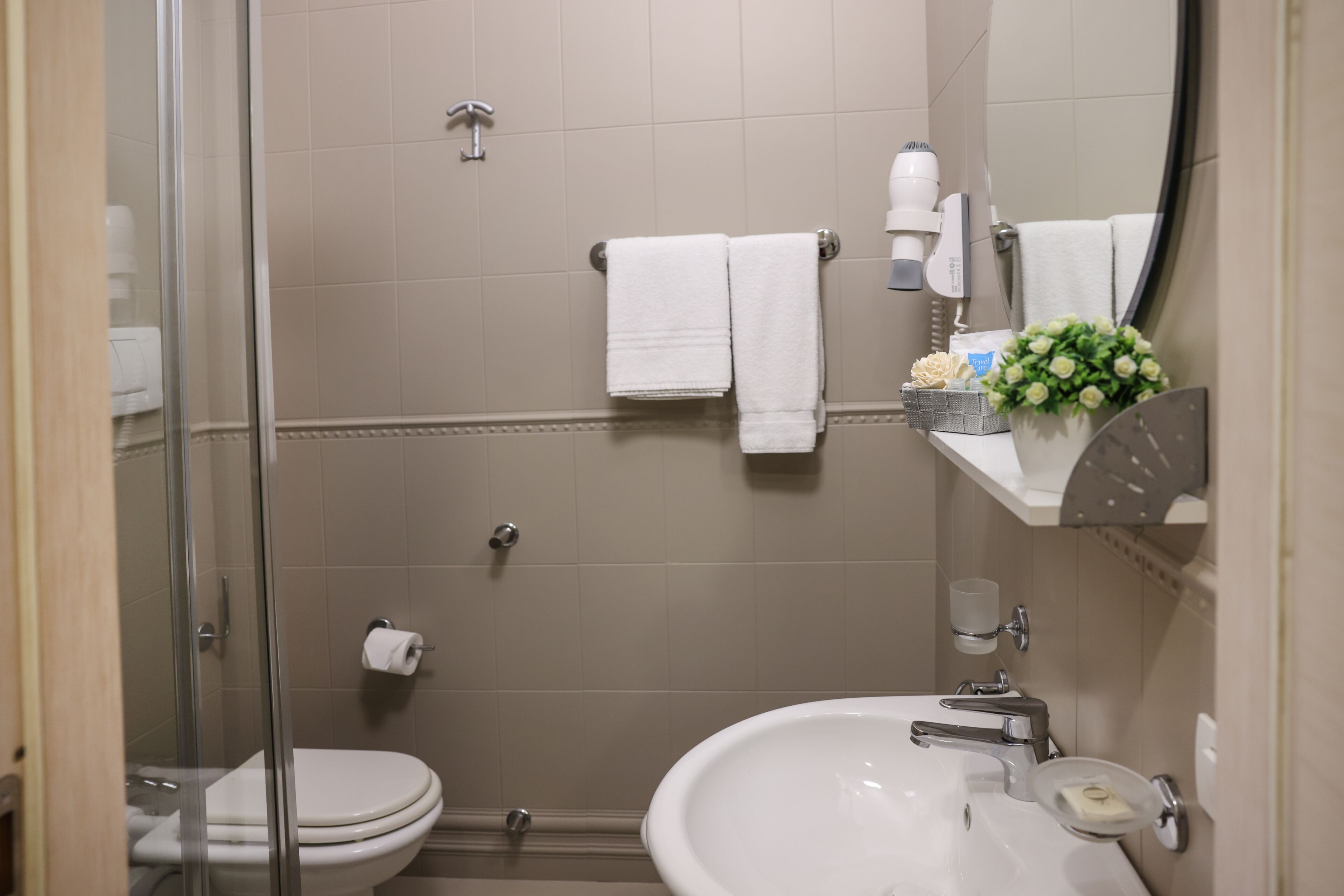 A bathroom with a glass shower enclosure, a toilet, a sink with a mirror, and a towel rack with two white towels.