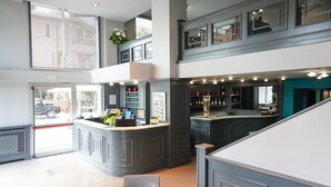 Een moderne hotel lobby met een centraal gelegen bar, zitgedeeltes en uitzicht op de straat.