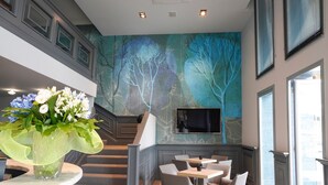 Een moderne hotellobby met een trap, zithoek en een groot muurdecor.