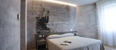A modern bedroom with a large bed, a nightstand, a wall-mounted artwork, and a window with curtains.