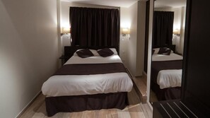 Habitación de hotel con una cama grande, cortinas oscuras, una mesita de noche y un espejo.