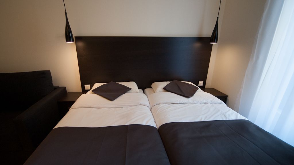 A modern hotel room with two beds, dark headboard, and bedside lamps.