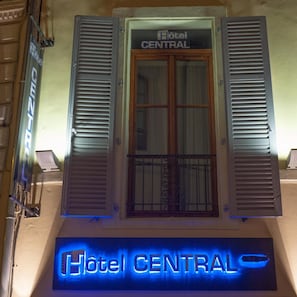 L’entrée d’un hôtel, avec une enseigne indiquant « Hôtel CENTRAL » et, en dessous, une enseigne lumineuse au néon.