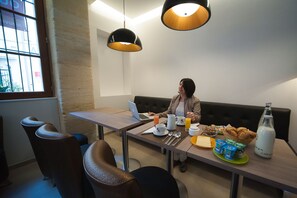 Una persona sentada a una mesa con un ordenador portátil, alimentos para el desayuno y una botella de leche.
