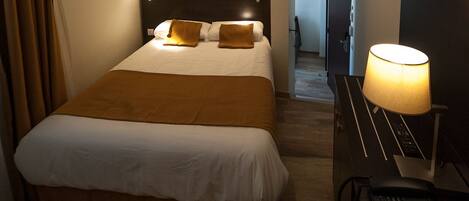 A hotel room with a large bed, a bedside table with a lamp, and a telephone.