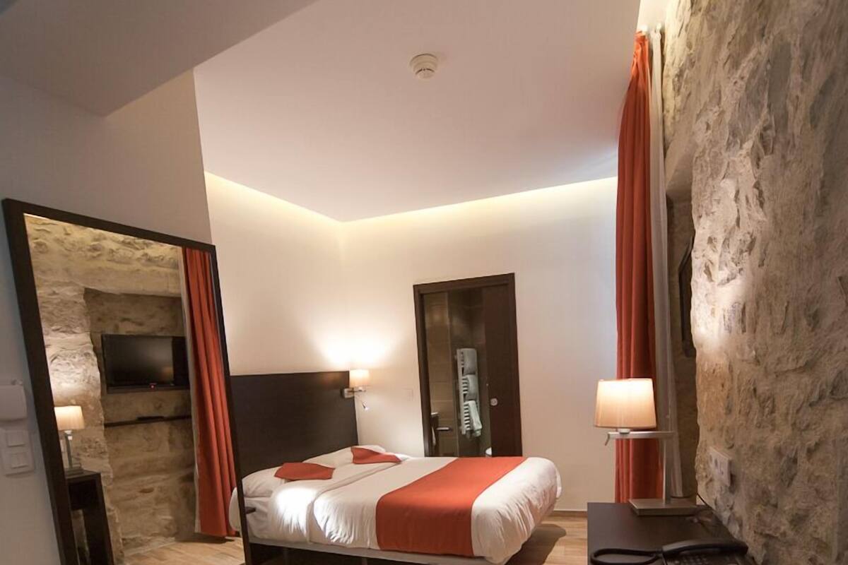 Una habitación de hotel moderna con una cama grande, un escritorio con teléfono, un espejo y una pared decorada con piedra.