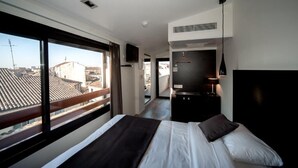 Quarto de hotel moderno com uma cama grande, uma kitchenette pequena e uma varanda com vista para a cidade.