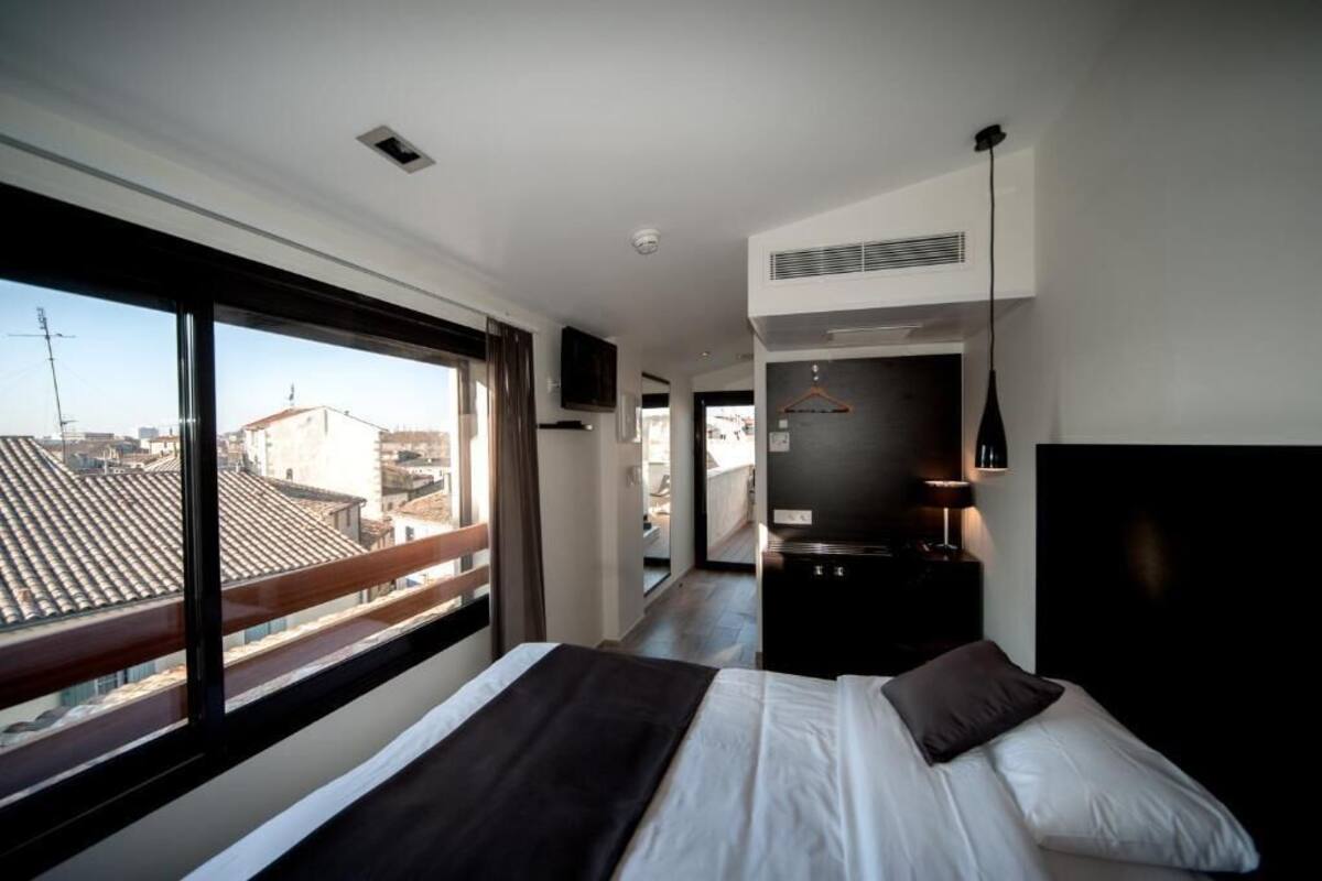 Una habitación de hotel moderna con una cama grande, una kitchenette pequeña y un balcón con vistas a la ciudad.