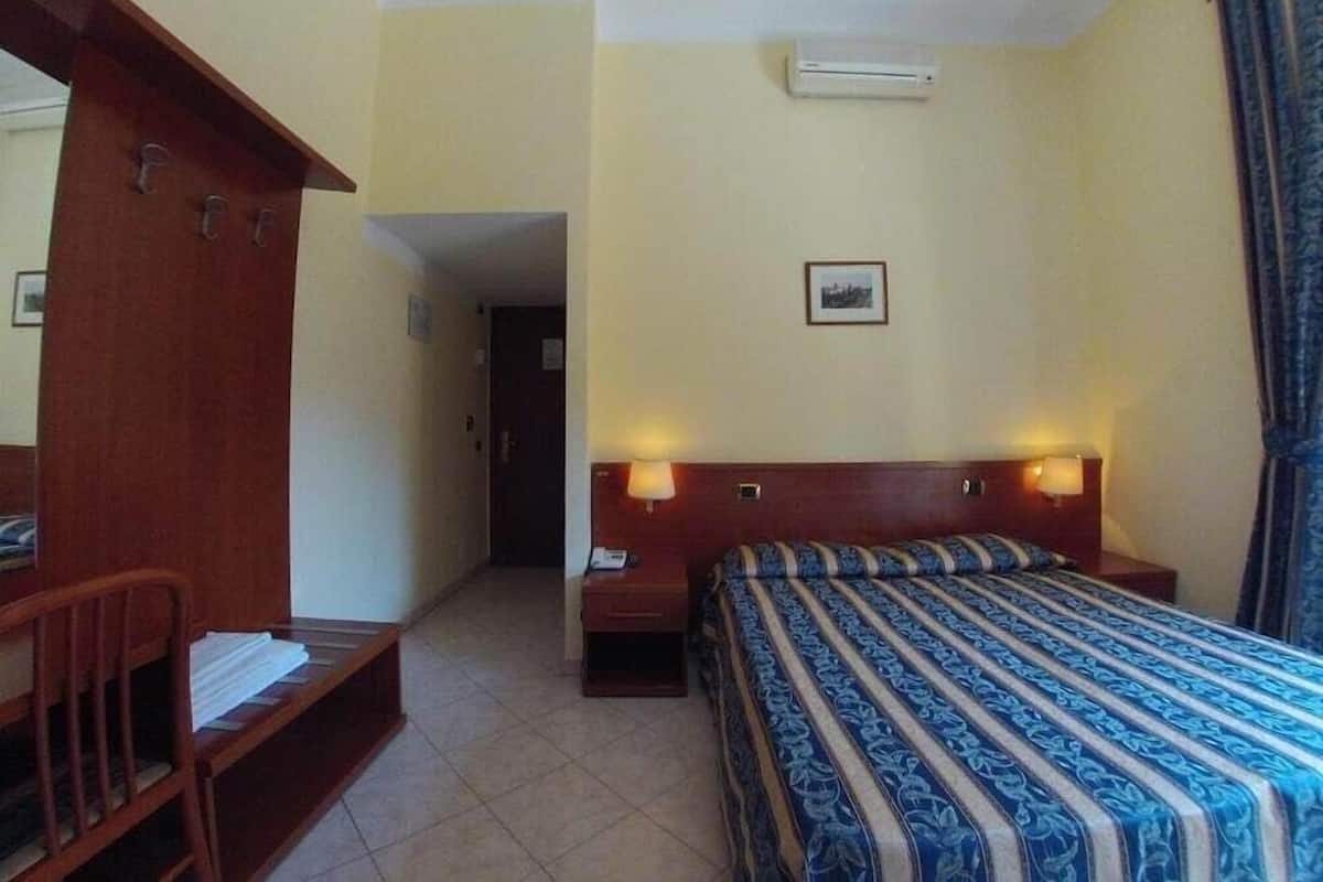 Habitación de hotel con una cama, un banco de madera, una mesita de noche y aire acondicionado instalado en la pared.