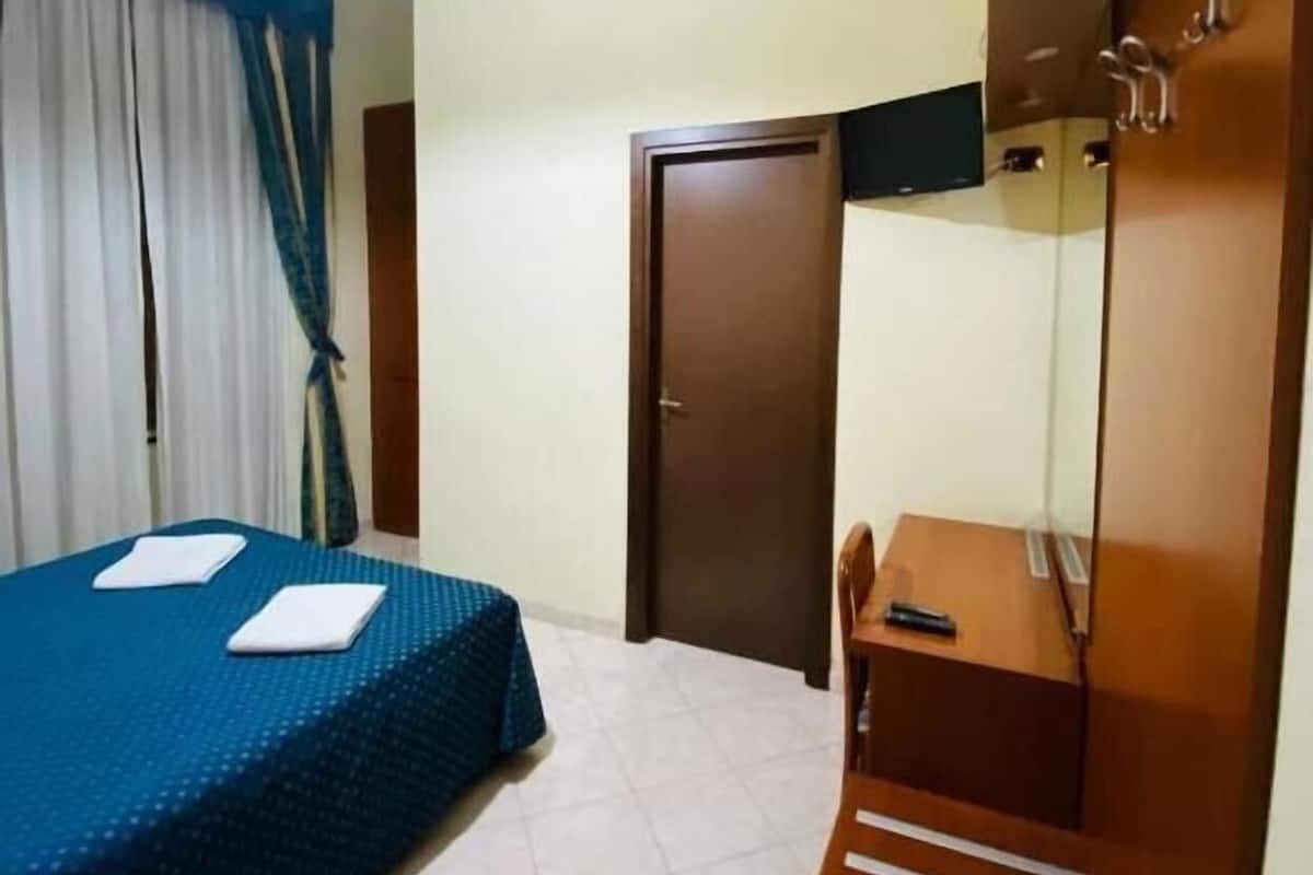 Una habitación de hotel con cama, escritorio, armario y puerta.