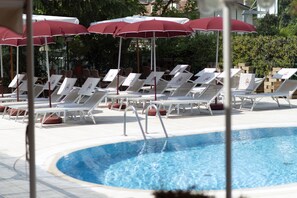 A pool area with white lounge chairs and red umbrellas. - Imperial (Garda)