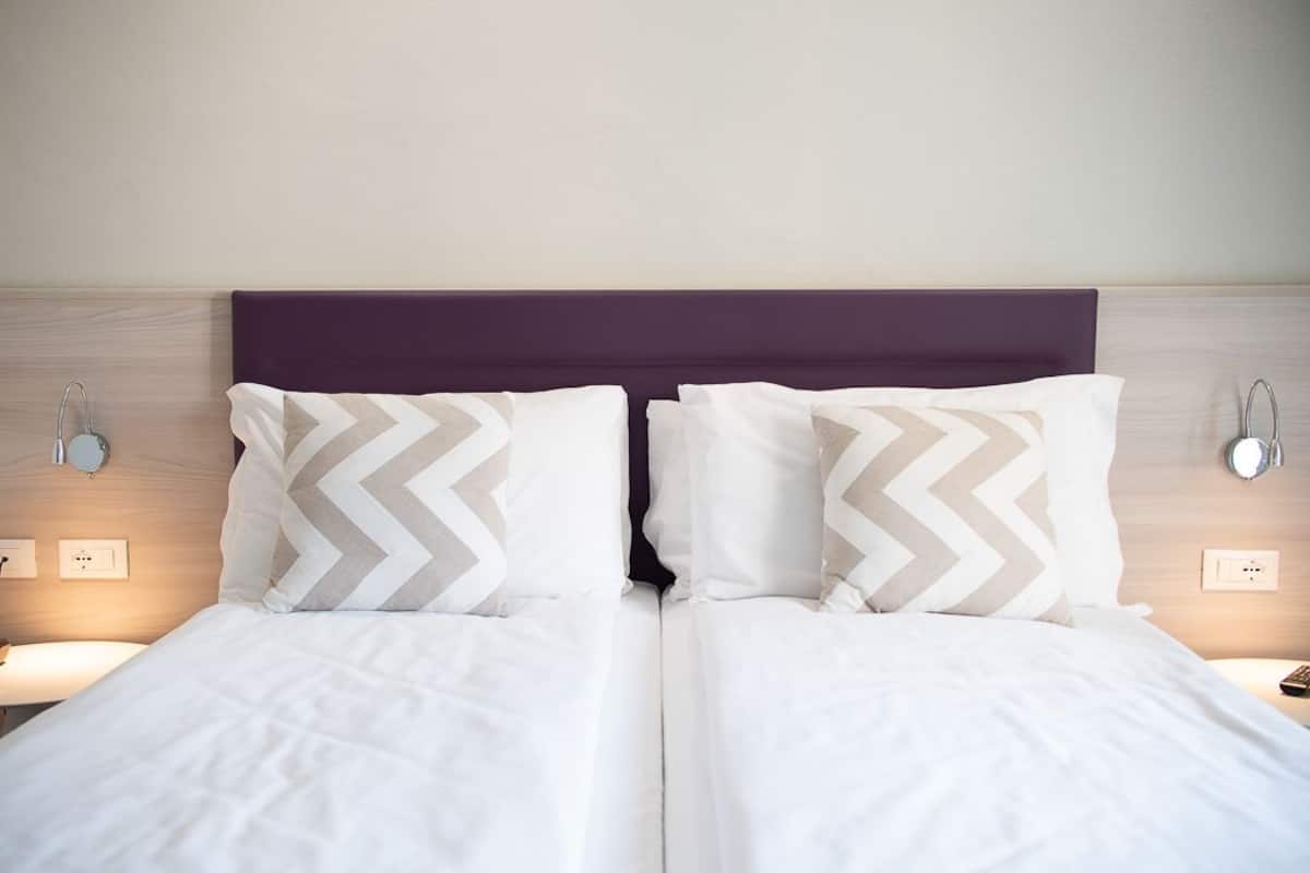 Un lit double avec une tête de lit violette, deux tables de chevet avec des lampes et un luminaire fixé au mur.