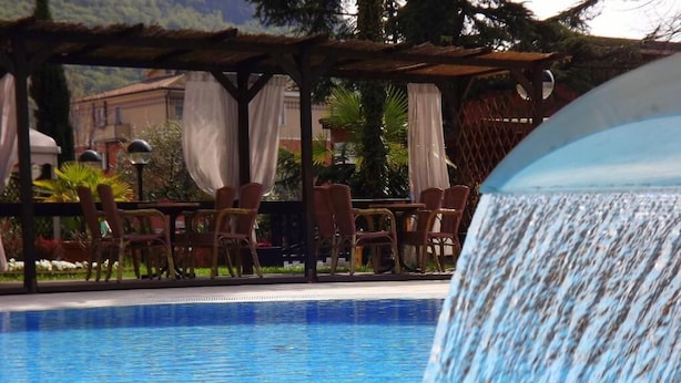 A pool area with a water feature, lounge chairs, and a covered seating area. - Imperial (Garda)
