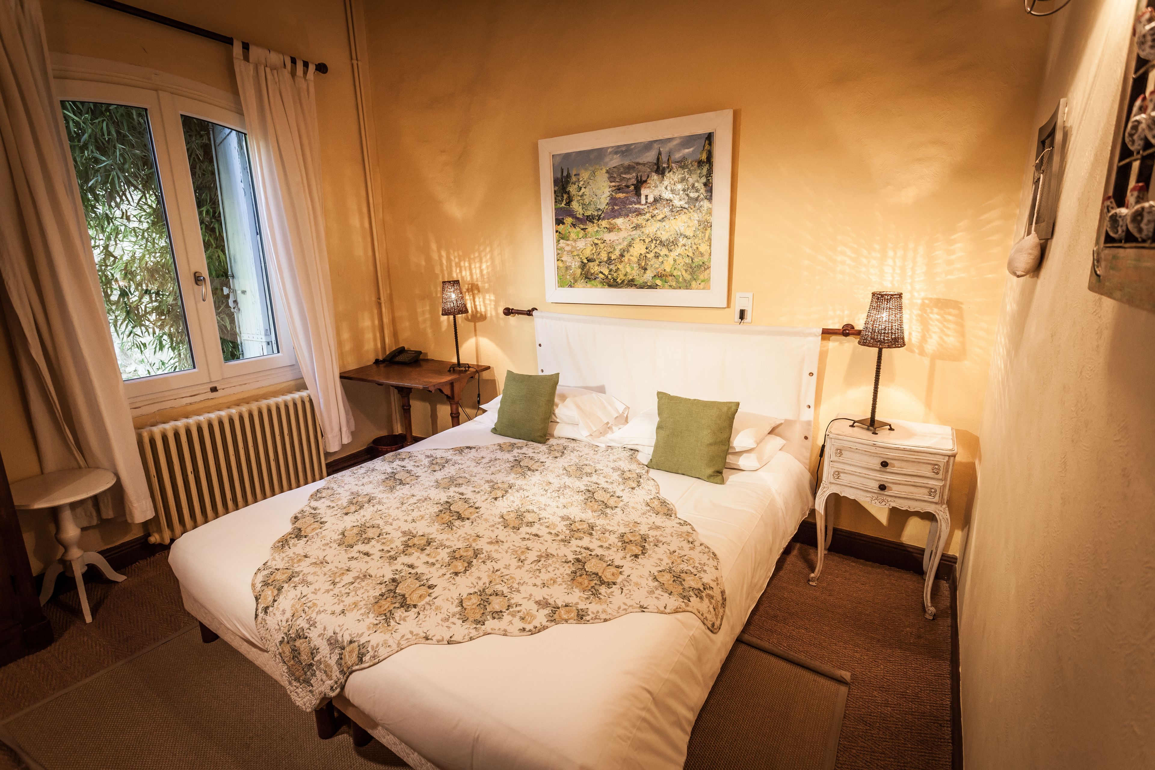 Un dormitorio con cama, dos mesitas de noche, un radiador y una ventana con cortinas.