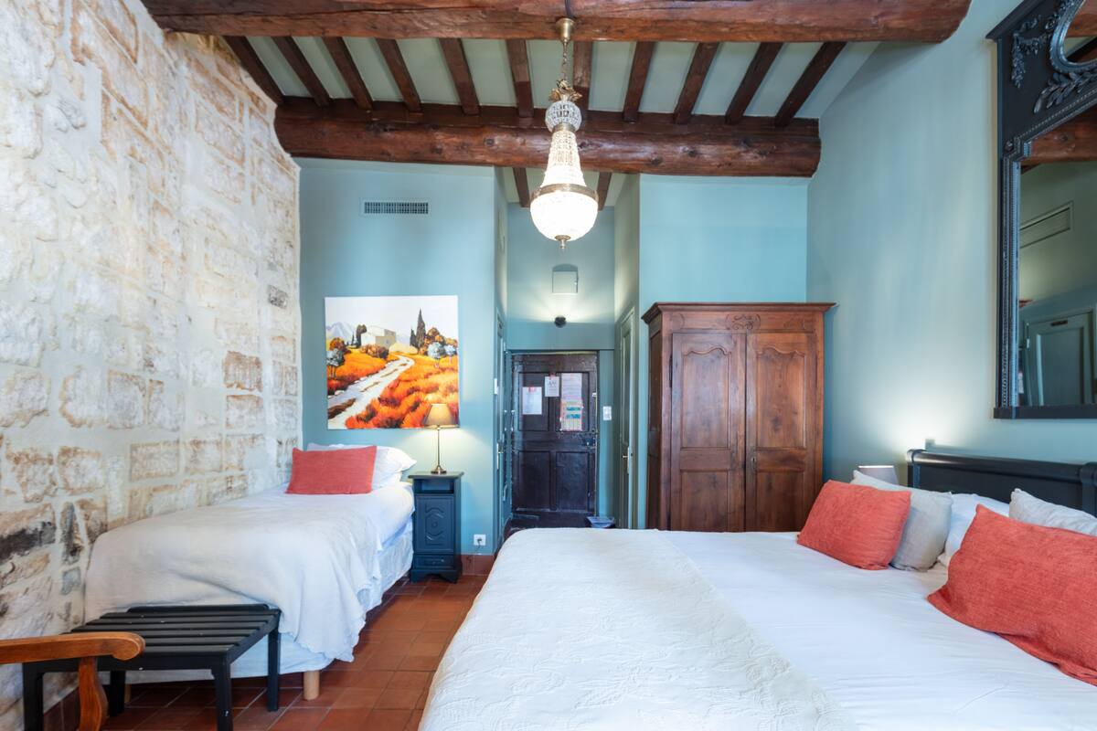 Une chambre à coucher avec un grand lit, deux tables de chevet, un banc en bois, une armoire et un lustre.