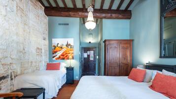 A bedroom with a large bed, two bedside tables, a wooden bench, a wardrobe, and a chandelier.