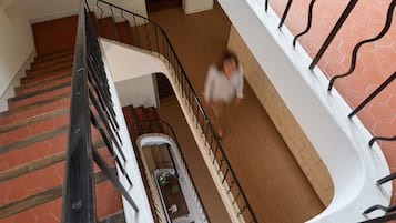 Un intérieur à plusieurs niveaux avec un escalier, un coin repas comprenant une table et des chaises, et un mur blanc orné d’un motif hexagonal.