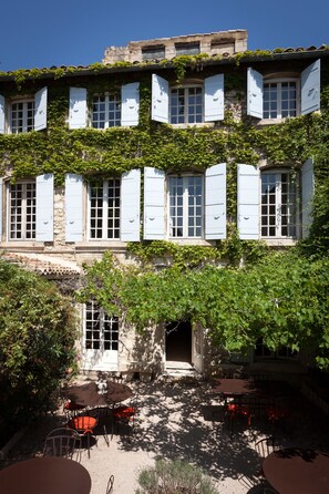 A building with multiple windows, some with shutters, and an outdoor seating area with tables and chairs. - Hôtel De l'Atelier (Villeneuve-les-Avignon)