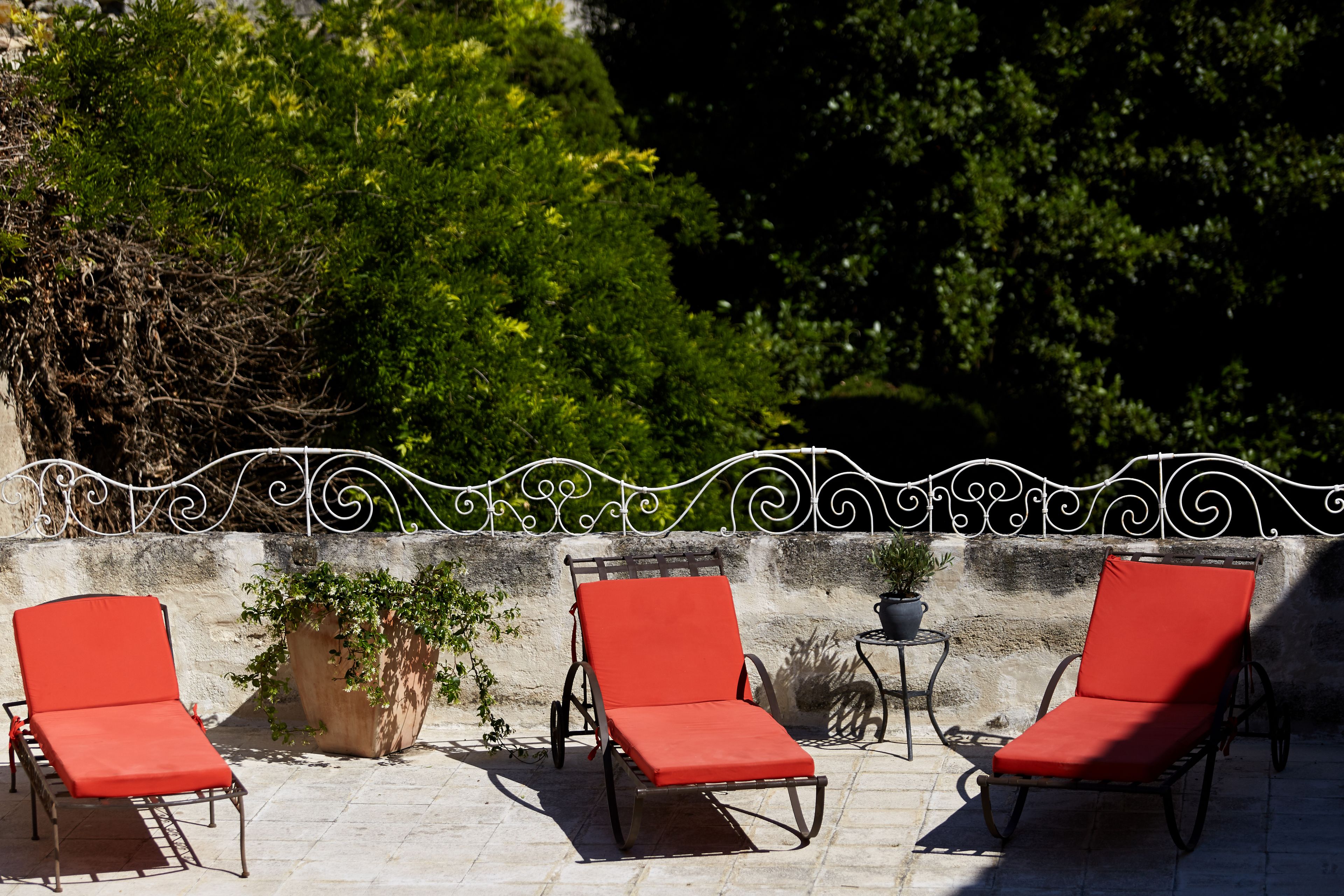 Three red lounge chairs with metal frames, positioned on a stone patio with a decorative metal railing in the background.