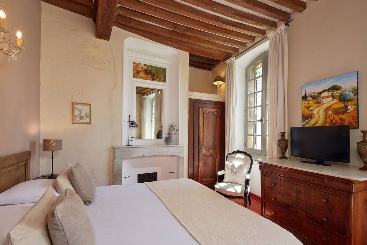 Une chambre à coucher comprenant un lit, une chaise, une commode, un téléviseur et un tableau accroché au mur.