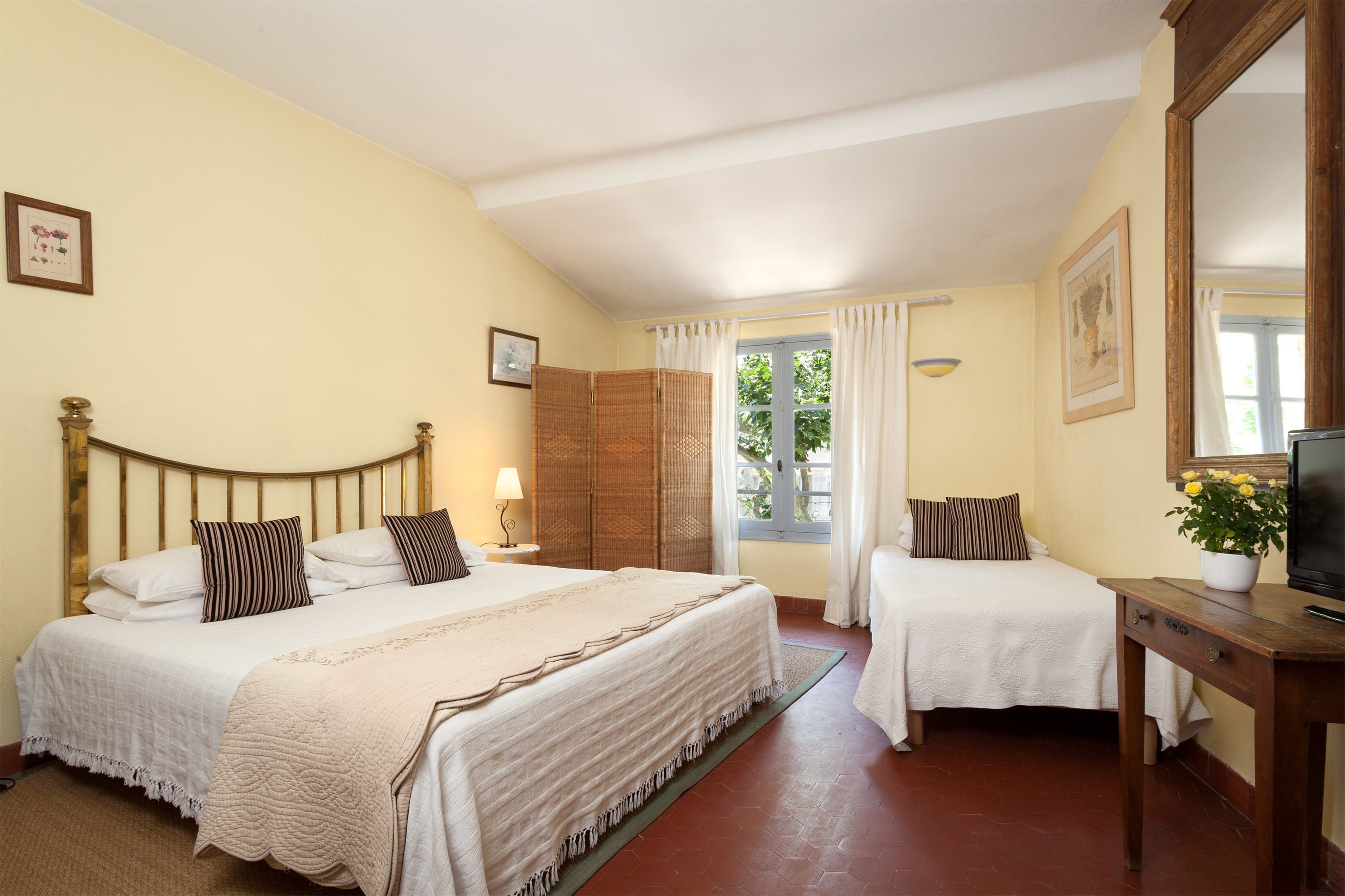 A hotel room with two beds, a television, and a window with curtains.