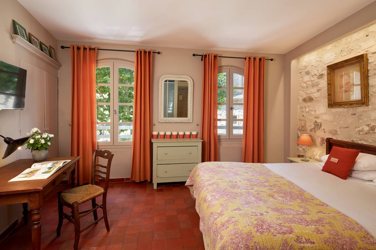 Une chambre à coucher avec un lit, un bureau avec une chaise, une commode et une fenêtre avec des rideaux.