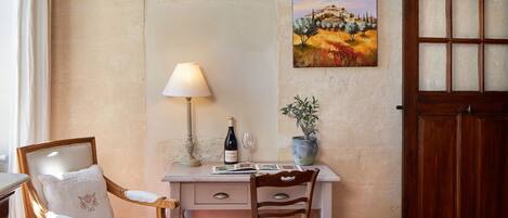 A bedroom with a bed, a desk with a lamp, a chair, a wooden door, and a painting on the wall.