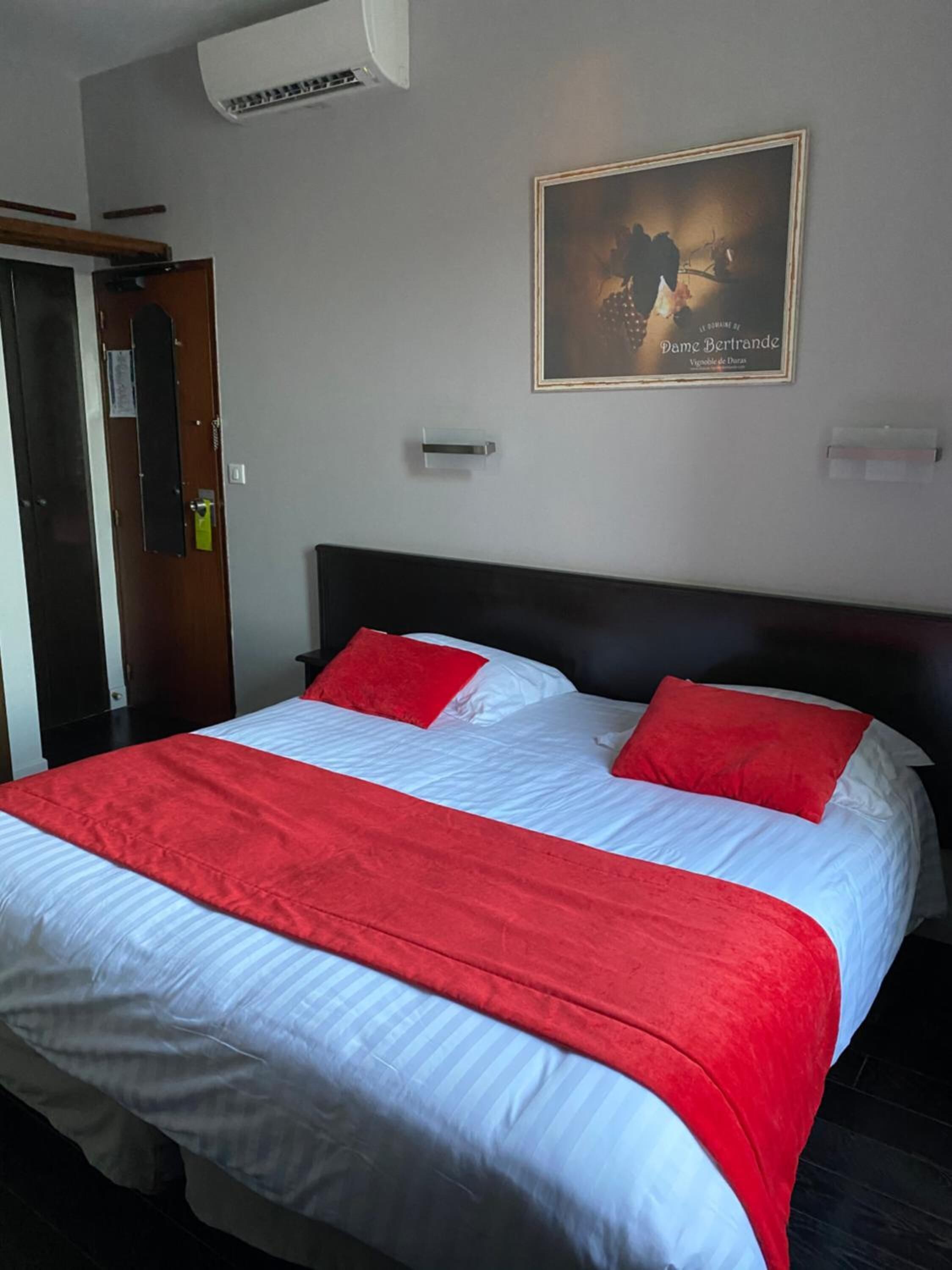 A hotel room with a bed, a door, and a framed picture on the wall.