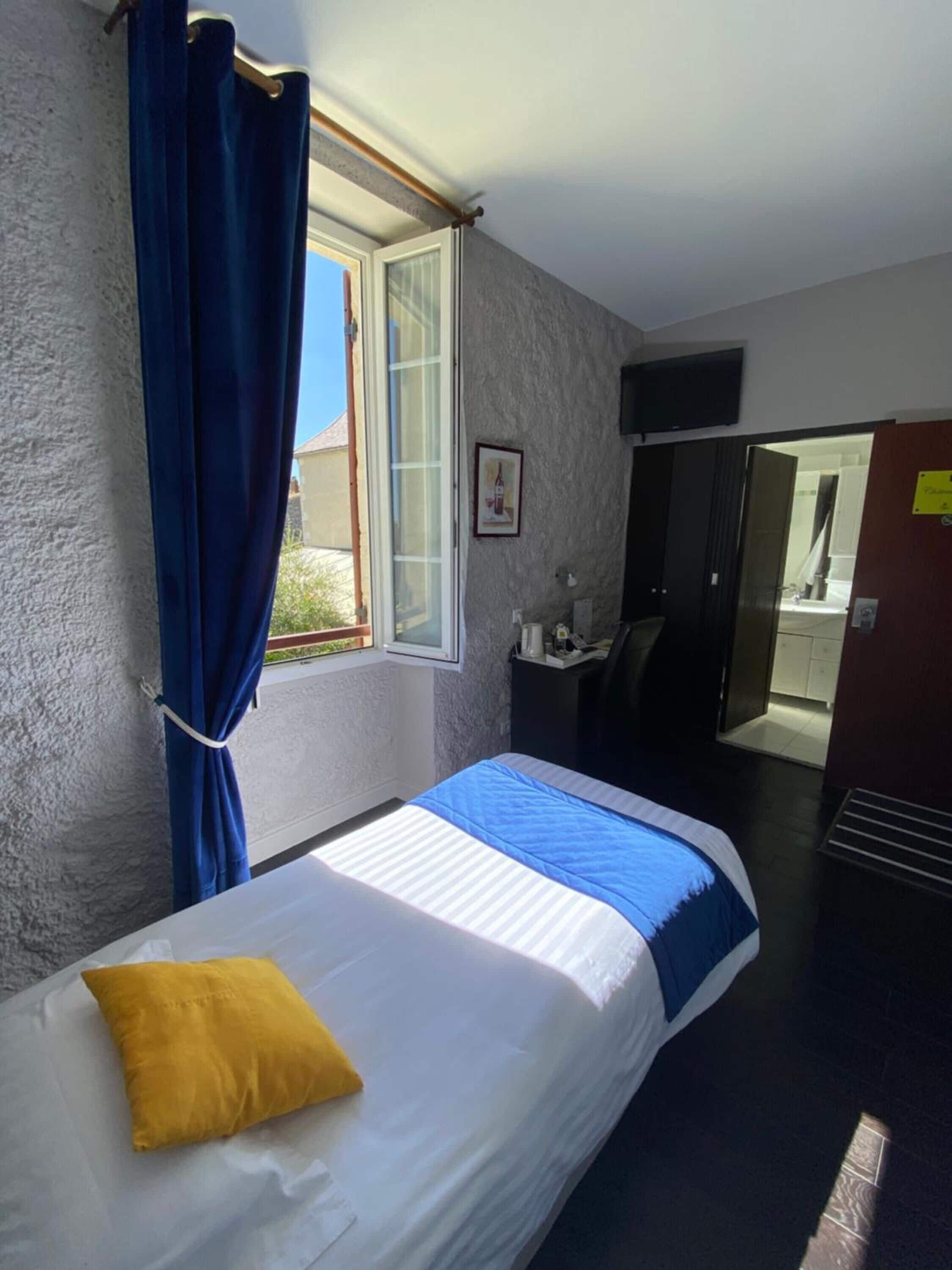 A bedroom with a bed, a window with curtains, a TV on the wall, and a door leading to another room.