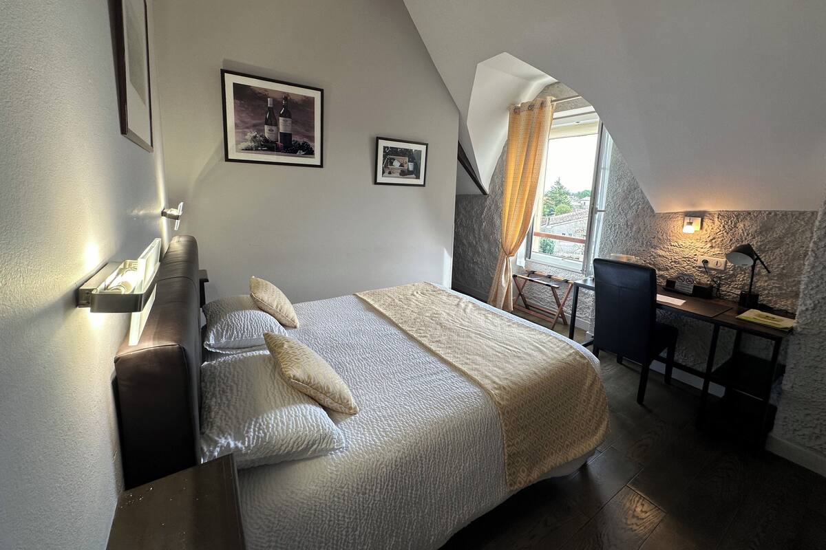 Quarto com cama, escrivaninha e janela com cortinas.