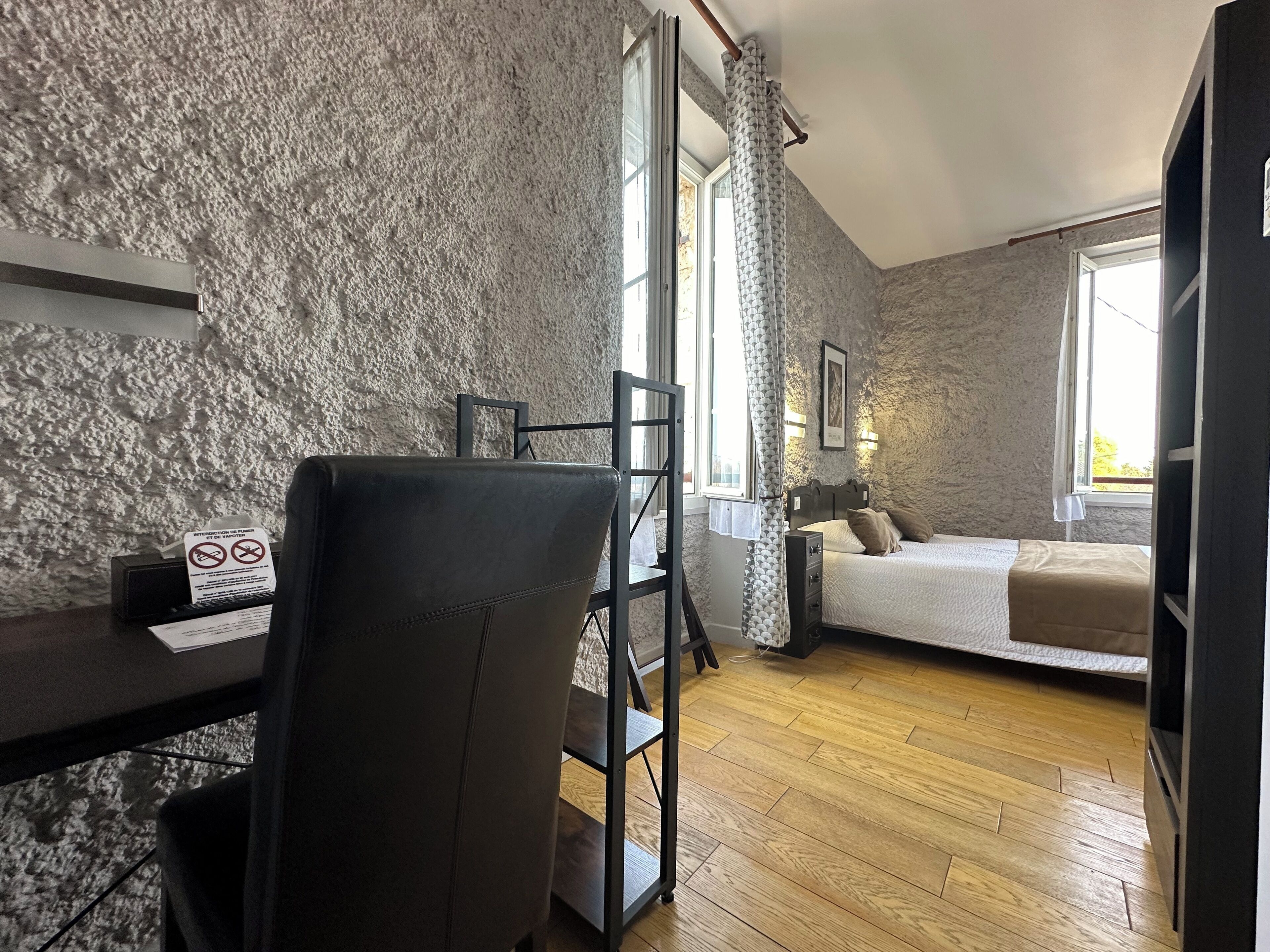 A room with a wooden floor, a desk with a chair, a bed with pillows, and a stone wall.
