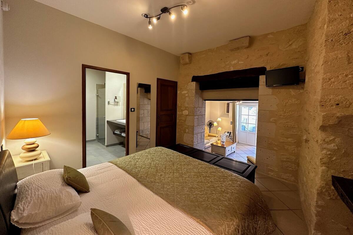 Quarto com cama, mesa de cabeceira, luminária e vista para um banheiro e uma sala de estar.
