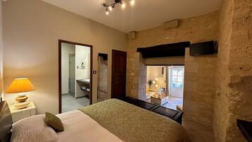 A bedroom with a bed, a nightstand, a lamp, and a view of a bathroom and a living area.