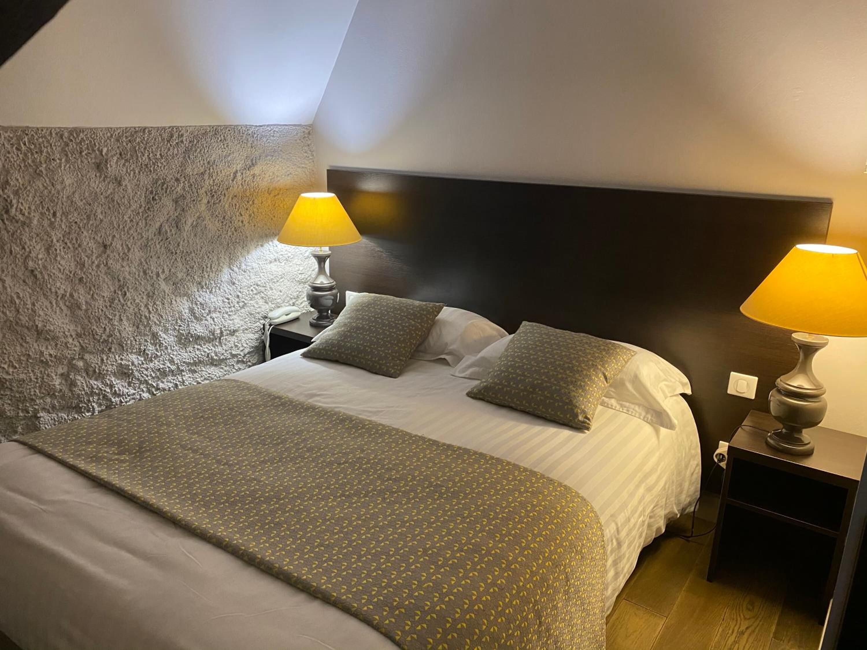 Une chambre d’hôtel avec un lit, deux lampes de chevet, un mur à motifs et une tête de lit sombre.