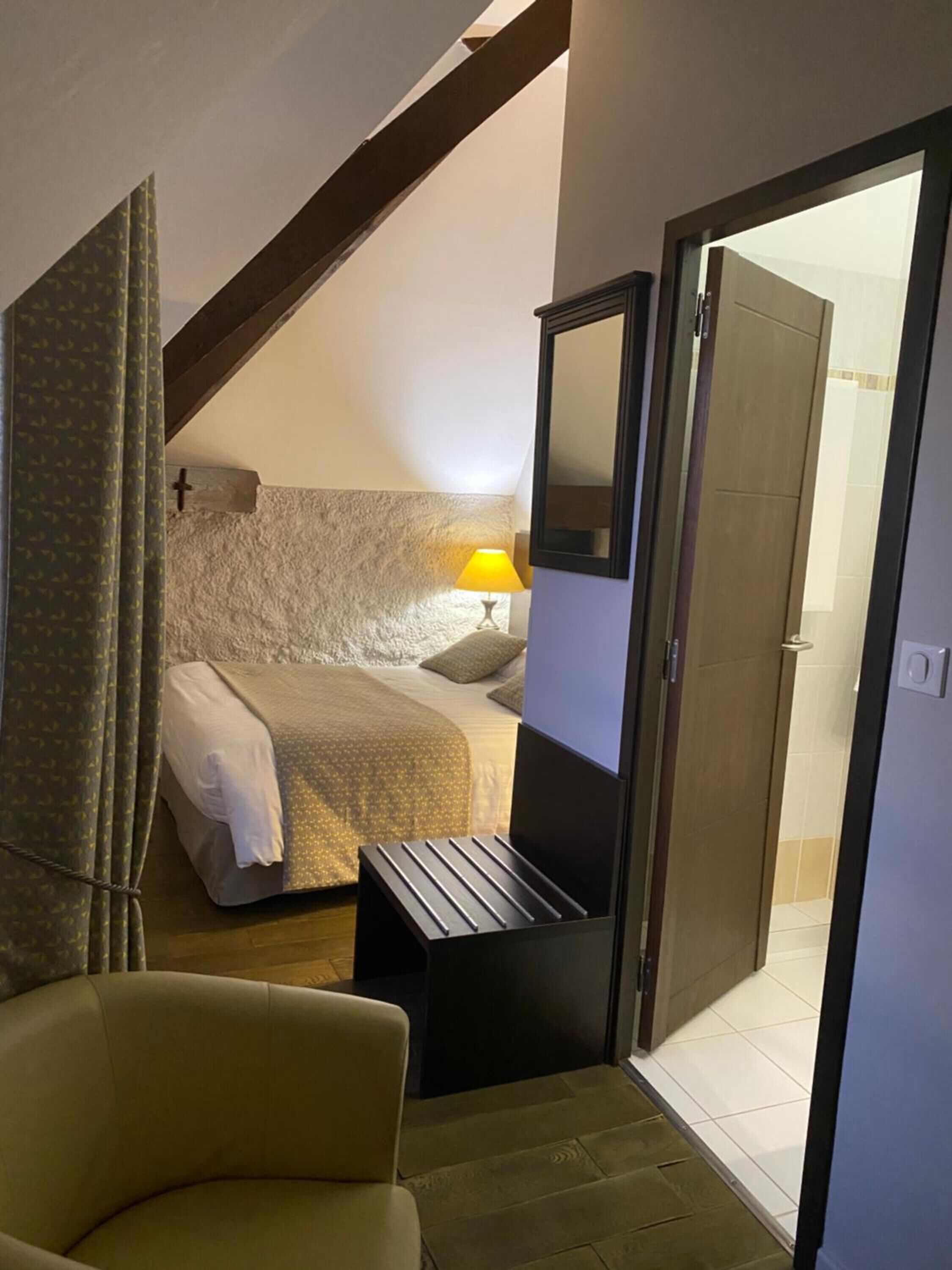 Un dormitorio con cama, una silla, una mesita de noche, una lámpara y un espejo.