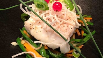 A dish with white fish, green vegetables, and red berries on a dark plate.