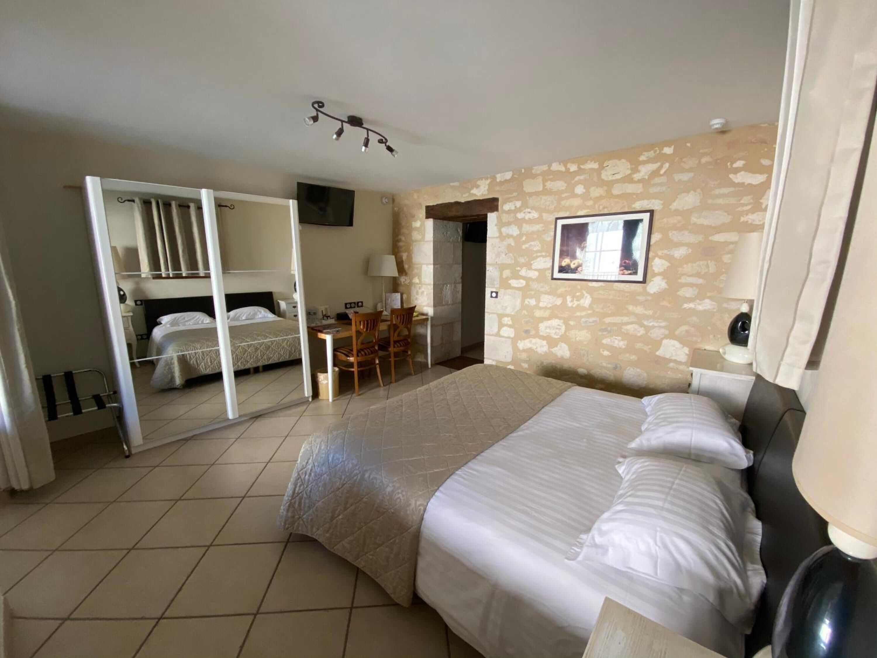 Une chambre d’hôtel avec un lit, un bureau, une chaise, une télévision et un mur en pierre.