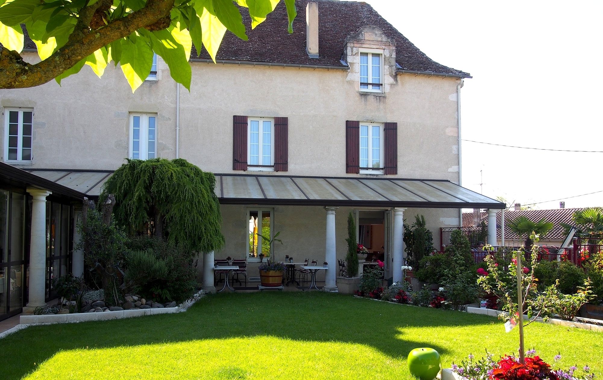 A two-story house with a covered patio, a well-maintained lawn, and a variety of plants and flowers.