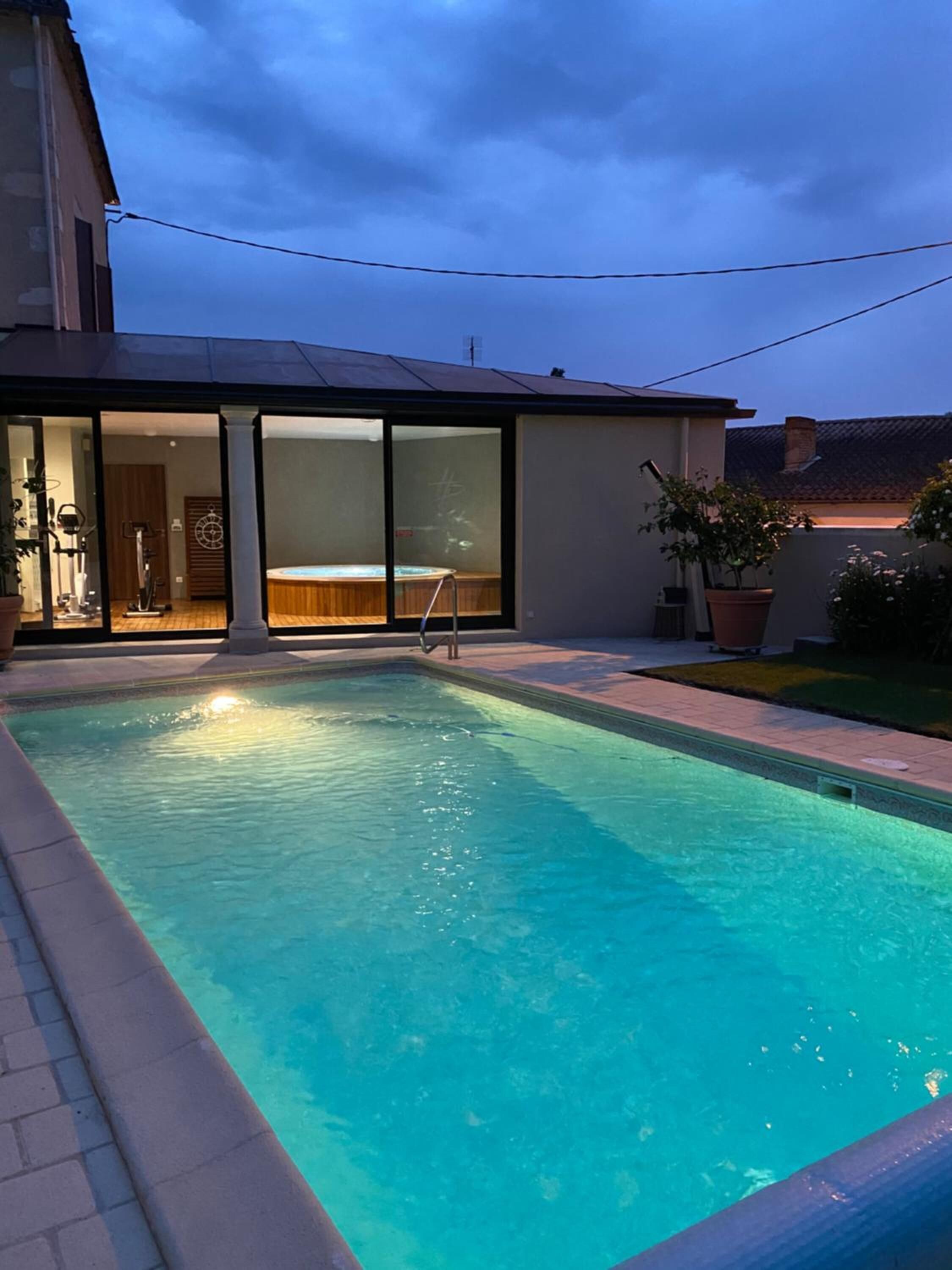 Une piscine avec un jacuzzi, un patio couvert et une vue sur l’intérieur.