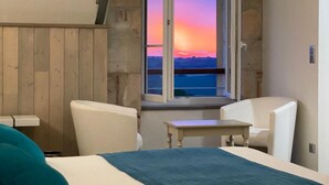 A bedroom with a large bed, a small table, two chairs, and a window with a sunset view. - LOGIS Hostellerie des Ducs (Duras)
