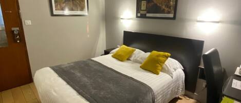 A bedroom with a bed, two pillows, a desk, and two framed pictures on the wall.
